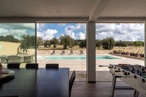 Un espacio interior moderno con vista a la piscina, una mesa de fútbol y un comedor.