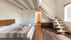 Un dormitorio con cama de cabecera de madera, colcha estampada, escalera de madera y cesta de mimbre.