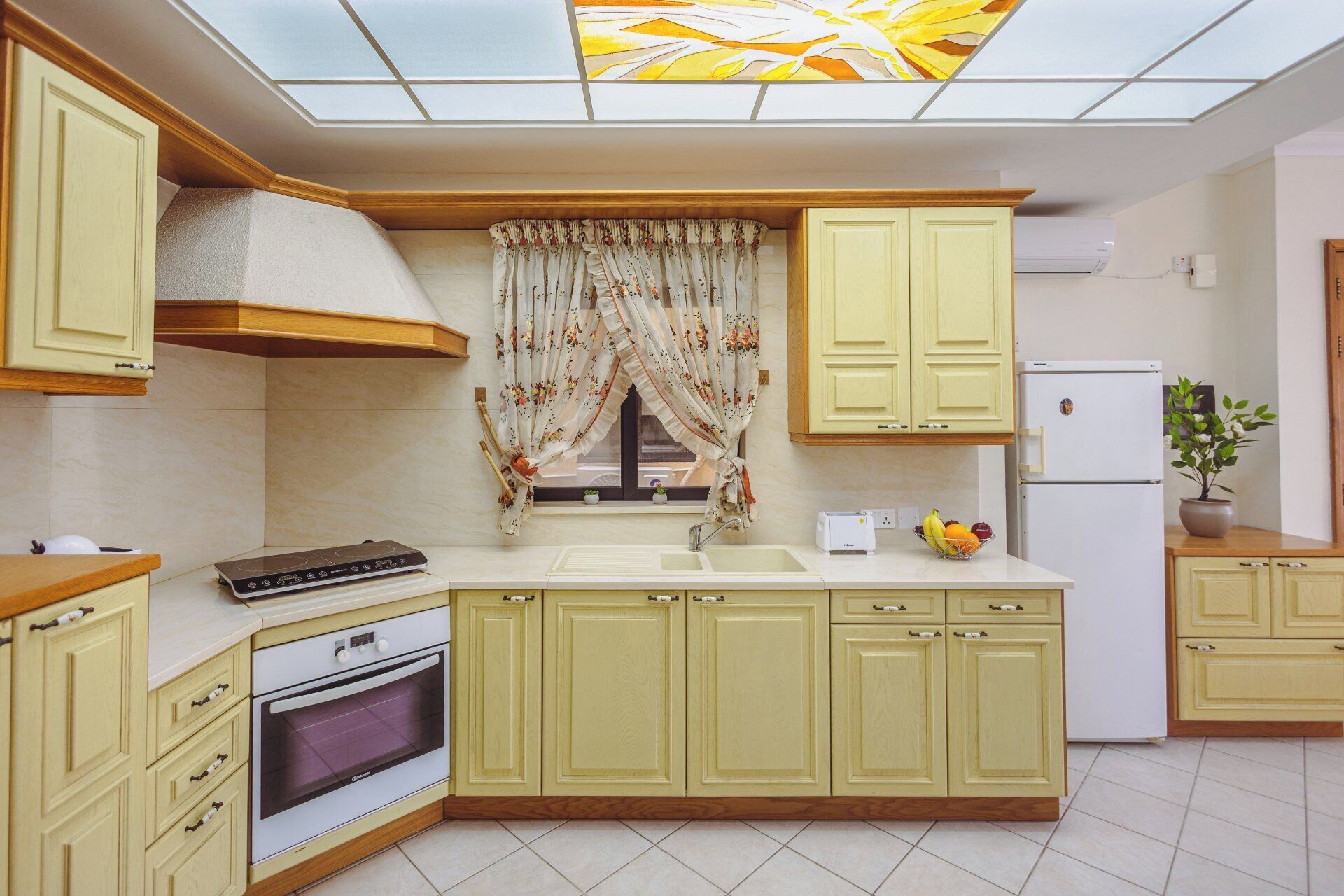 Eine Küche mit Backofen, Spüle, Kühlschrank und einem Fenster mit blumigen Vorhängen.