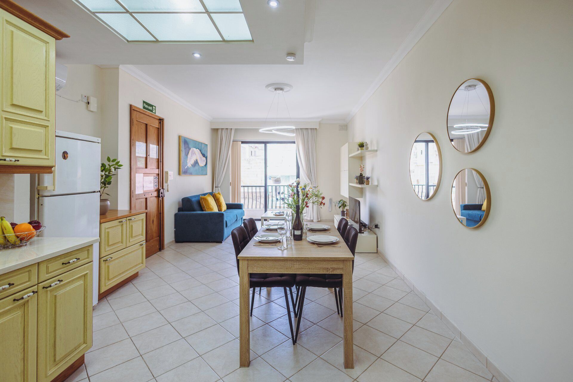 A modern kitchen with a dining area, a blue sofa, and a balcony with a view.