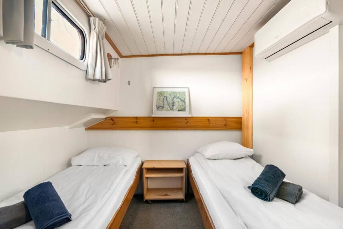 A small, compact room with two single beds, a small table, a shelf, and a window.