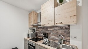 Una cocina compacta con armarios de madera, un lavamanos de acero inoxidable, un microondas y una cafetera.