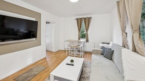 Una sala de estar moderna con un televisor de pantalla plana, un sofá, una mesa de centro, una mesa de comedor con sillas y una ventana con cortinas.