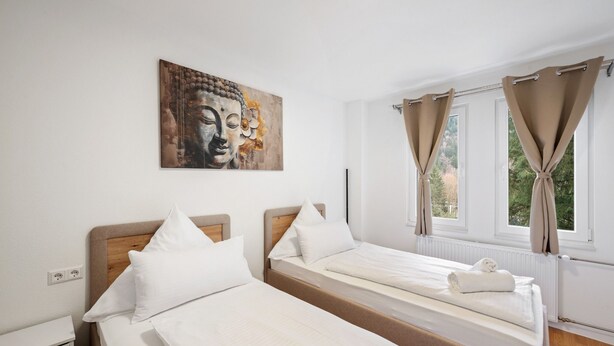 Habitación de hotel con dos camas, un cuadro de Buda colgado en la pared y una ventana con cortinas.