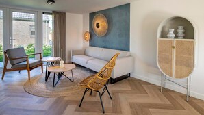 Een moderne woonkamer met een bank, twee stoelen, een salontafel, een decoratief wandobject en een rotan kast.
