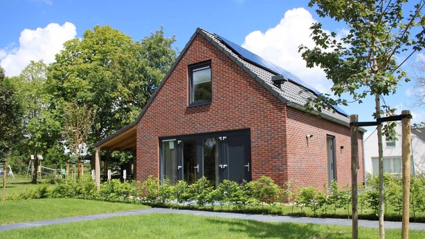 Een rode bakstenen woning met een schuin dak, een groot raam en een kleine deur.
