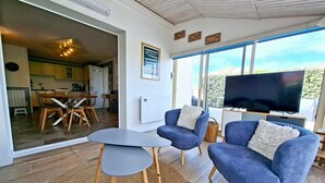 A modern living room with a TV, two blue armchairs, a small table, and a view of the kitchen and outside. - Holiday Home "La Maison De Marion" with Private Terrace, Wi-Fi, and Air Conditioning (La Tranche-sur-Mer)