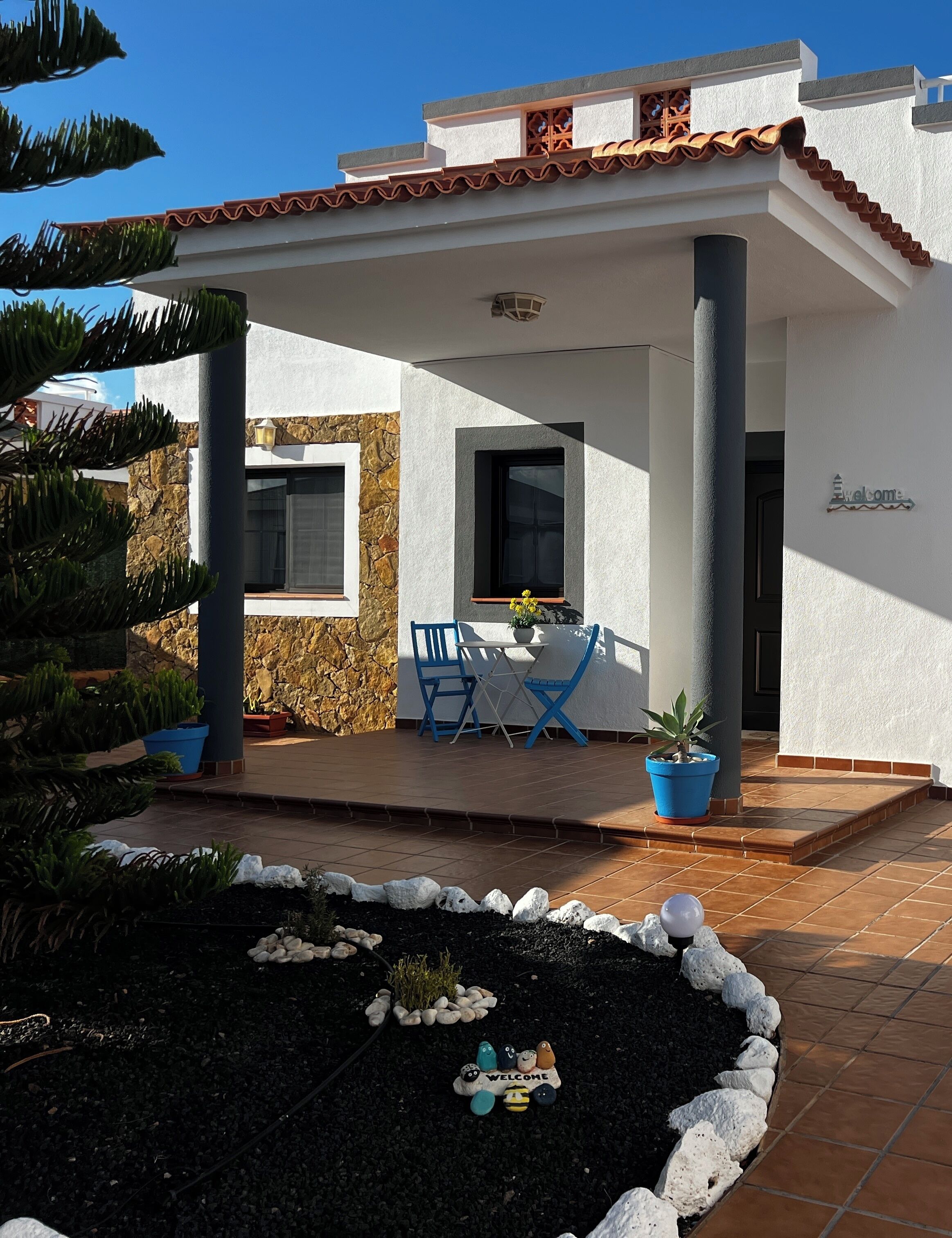 A modern house with a patio, a welcome sign, and a stone wall.