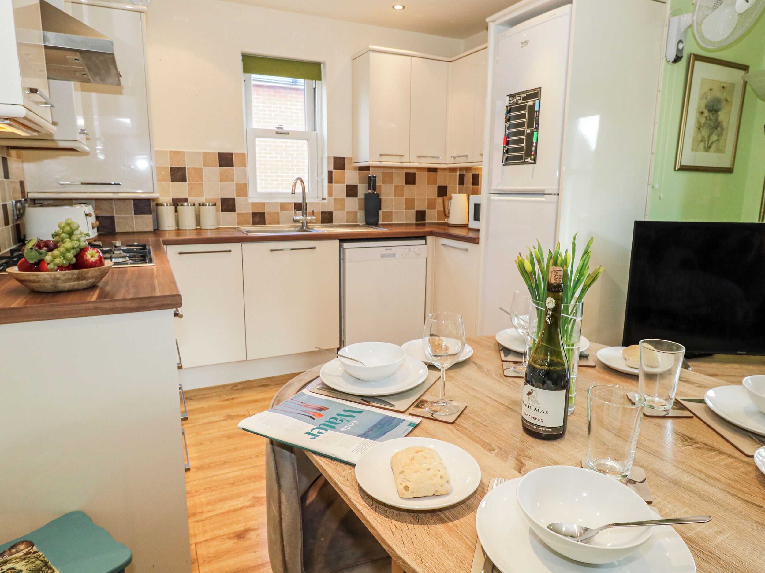 Una cocina moderna con armarios blancos, encimera de madera y un comedor con mesa preparada para dos.