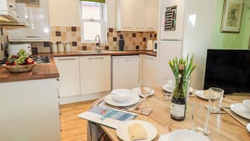 Una cocina moderna con armarios blancos, encimera de madera y un comedor con mesa preparada para dos.