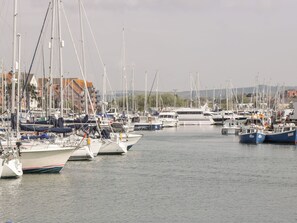A marina with multiple boats docked, buildings in the background, and a clear sky. - Rodwell Holt (Weymouth)
