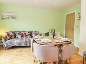 A dining area with a round table, chairs, a sofa, and a painting on the wall. - Rodwell Holt (Weymouth)