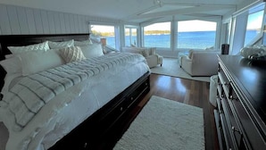 A bedroom with a large bed, two chairs, a dresser, and a view of the sea. - CASTLEWOOD COTTAGE - Town of Owls Head (Owls Head)