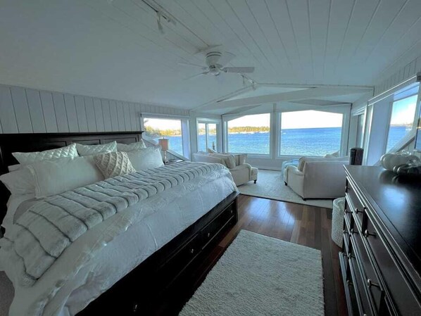 Un dormitorio con una cama grande, dos sillas, un tocador y vista al mar.