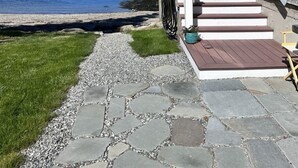 A wooden house with a stone pathway leading to a dock, overlooking a calm body of water. - CASTLEWOOD COTTAGE - Town of Owls Head (Owls Head)