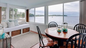 A dining area with a view of the water, a seating area with cushions, and a table with chairs. - CASTLEWOOD COTTAGE - Town of Owls Head (Owls Head)