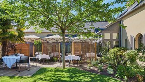An outdoor patio with tables and chairs, a wooden fence, and a garden area with various plants. - Maison KERVARREC (Saint-Gregoire)