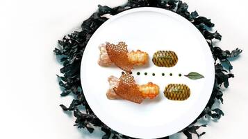 Un plato blanco con tres alimentos y una hoja decorativa sobre un fondo oscuro y frondoso.