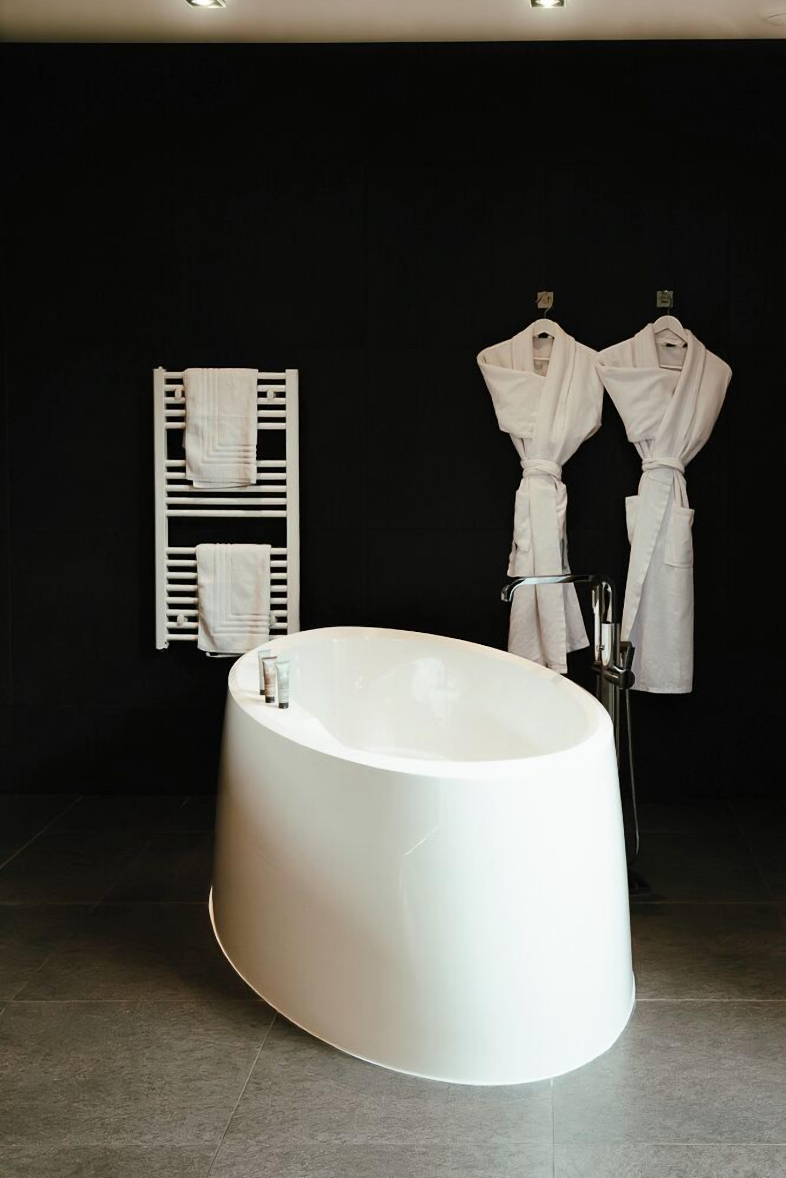 A modern bathroom with a freestanding bathtub, a towel rack with folded towels, and two robes hanging on hooks.