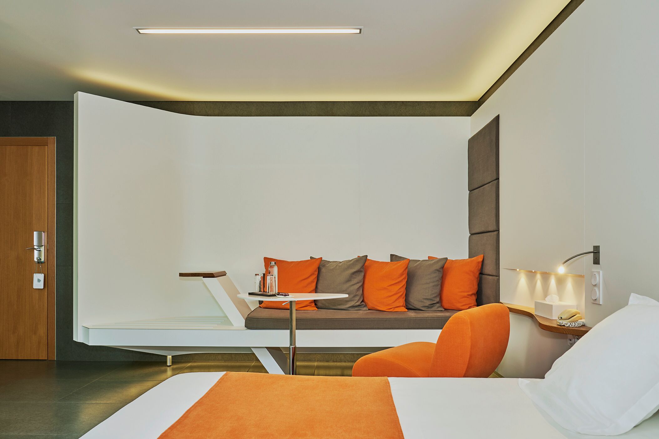 Una habitación de hotel moderna con un sofá, una mesita, una silla, una mesita de noche y una lámpara.