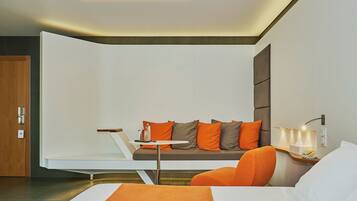 Una habitación de hotel moderna con un sofá, una mesita, una silla, una mesita de noche y una lámpara.