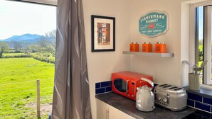 Eine Küche mit Blick auf ein grünes Feld, einer roten Mikrowelle, einem Wasserkocher, einem Toaster und einem Schild an der Wand.