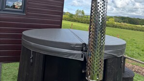 Ein Whirlpool mit Metallgitterabdeckung, einer Holzterrasse und Blick auf ein Wiesenfeld.
