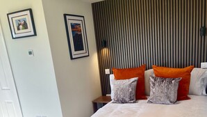Ein modernes Hotelzimmer mit einem großen Bett, orangefarbenen und weißen Kissen, einem Holterslatten-Kopfteil und gerahmten Bildern an den Wänden.