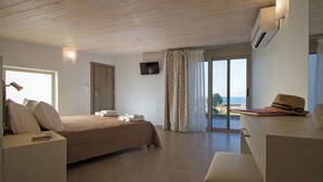 Une chambre à coucher comprenant un lit, une table de chevet, un bureau et une vue sur la mer, visible à travers une grande fenêtre.