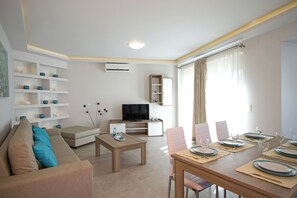 A modern living room with a sofa, coffee table, TV, and dining area set with plates and glasses. - Enali Villas-Mirti Villa (Kissamos)
