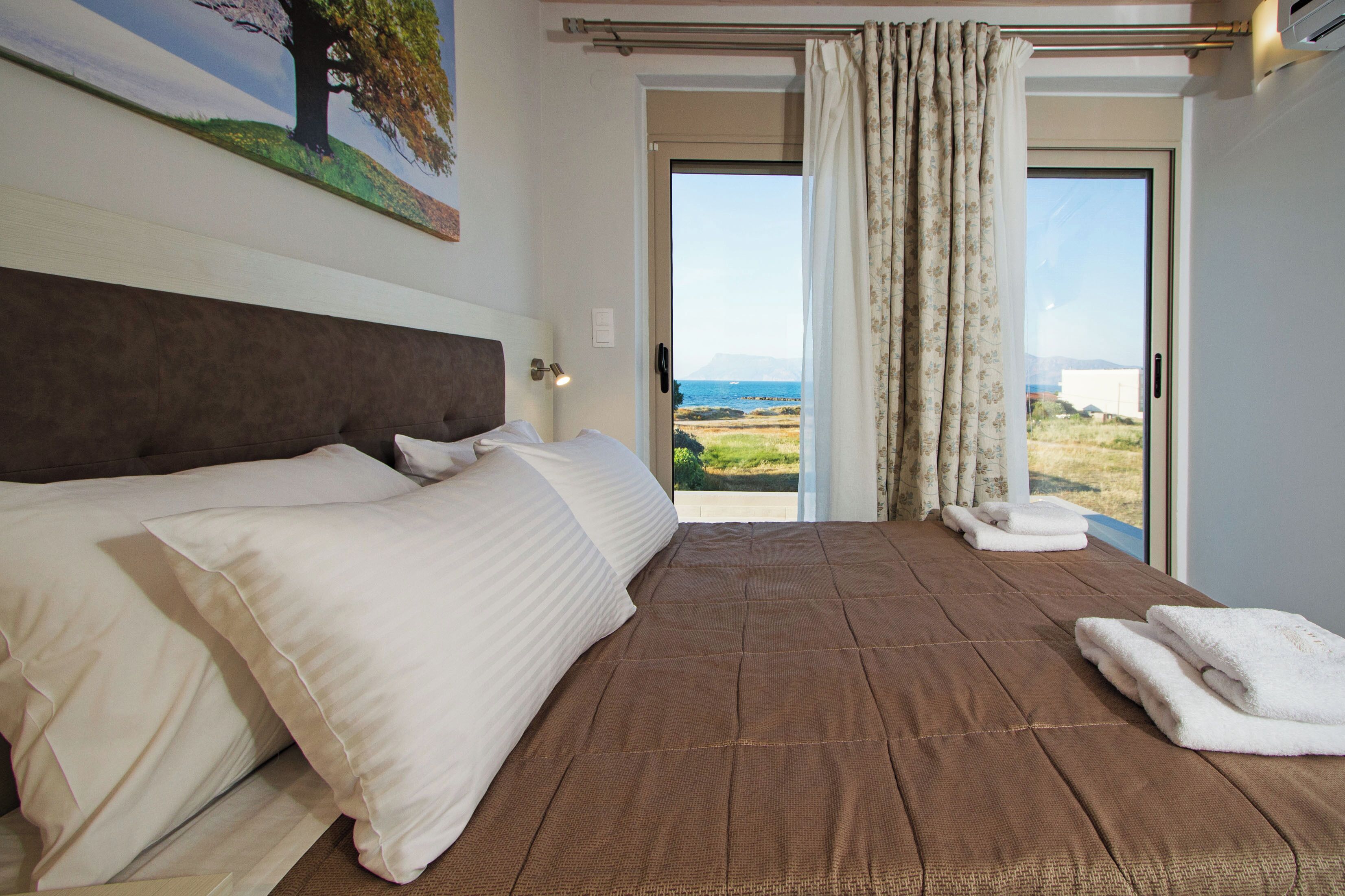 A bedroom with a large bed, a view of the outdoors, and a painting on the wall.