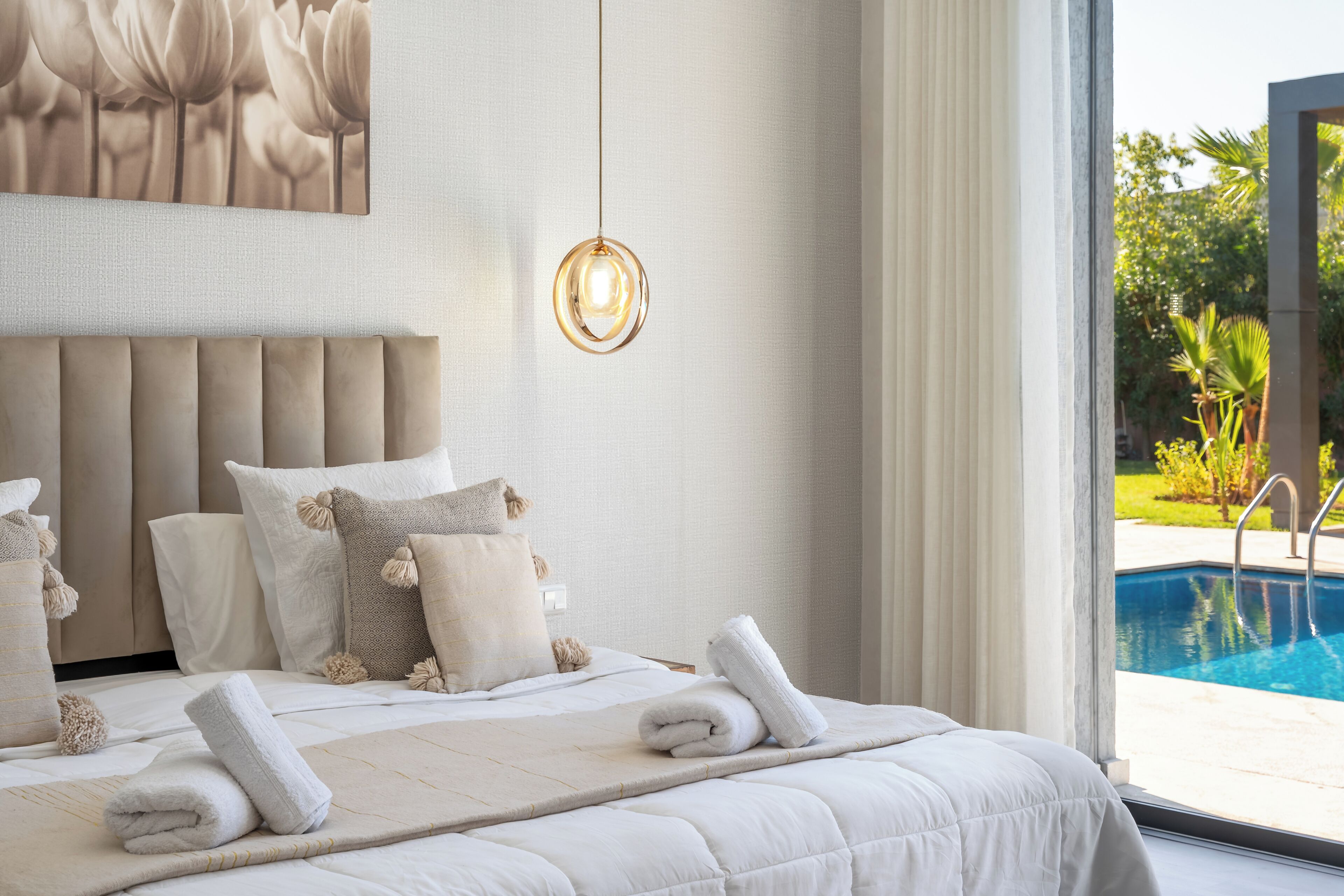 Une chambre avec un grand lit, un luminaire suspendu et une vue sur une piscine.
