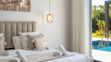Une chambre avec un grand lit, un luminaire suspendu et une vue sur une piscine.