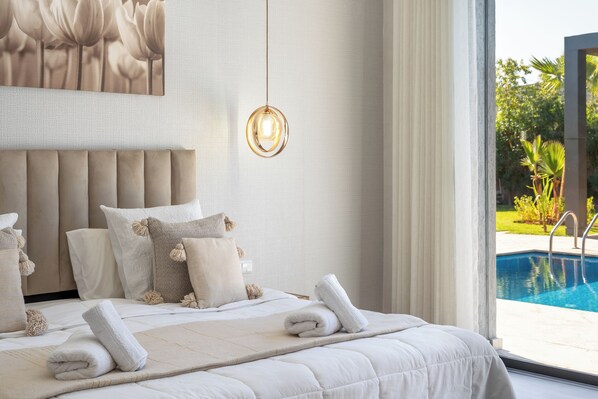 A bedroom with a large bed, a hanging light fixture, and a view of a swimming pool.