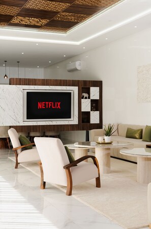 A modern living room with a large flat-screen TV, two armchairs, a coffee table, and a sofa.