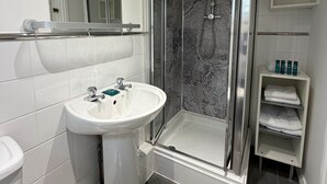 A modern bathroom with a white sink, a glass shower enclosure, and a white tiled floor. - Redlands (Bickenhill)
