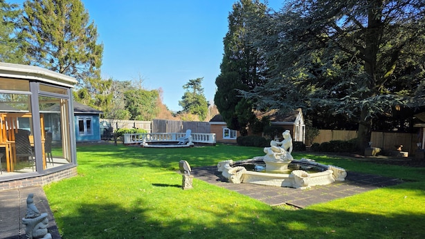 A backyard with a fountain, a glass-enclosed patio, and a lawn. - Redlands (Bickenhill)
