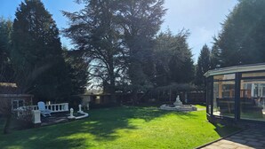 A backyard with a lawn, a fountain, and a glass-enclosed patio area. - Redlands (Bickenhill)