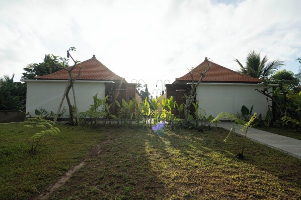 A two-story building with a tiled roof, surrounded by a garden with various plants and a paved pathway. - Taru Sebatu Villa (Sebatu)