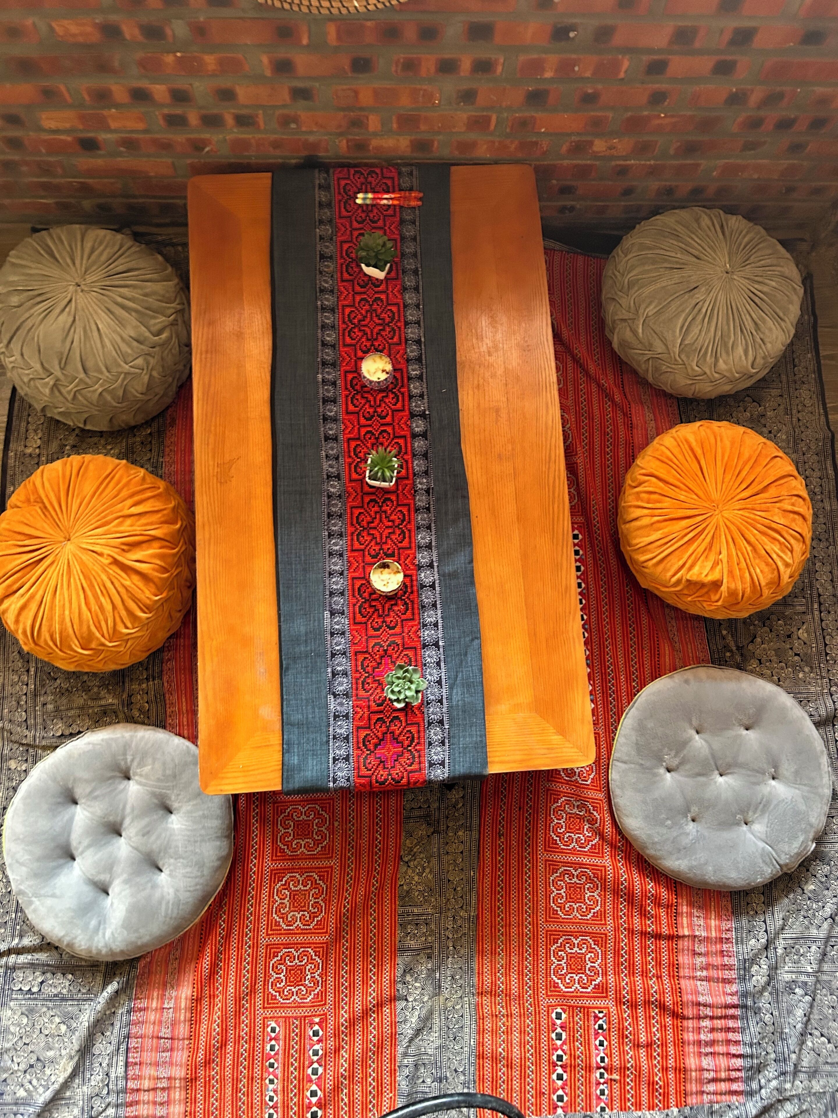 Una habitación con un tapete estampado, una mesa central decorada y dos otomanes redondos.