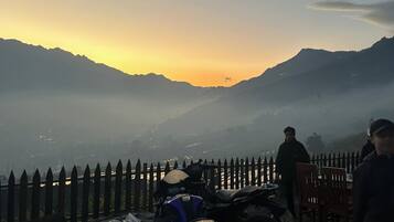 Blick auf einen Sonnenuntergang mit Bergen, einem Holzzaun und abgestellten Motorrädern.