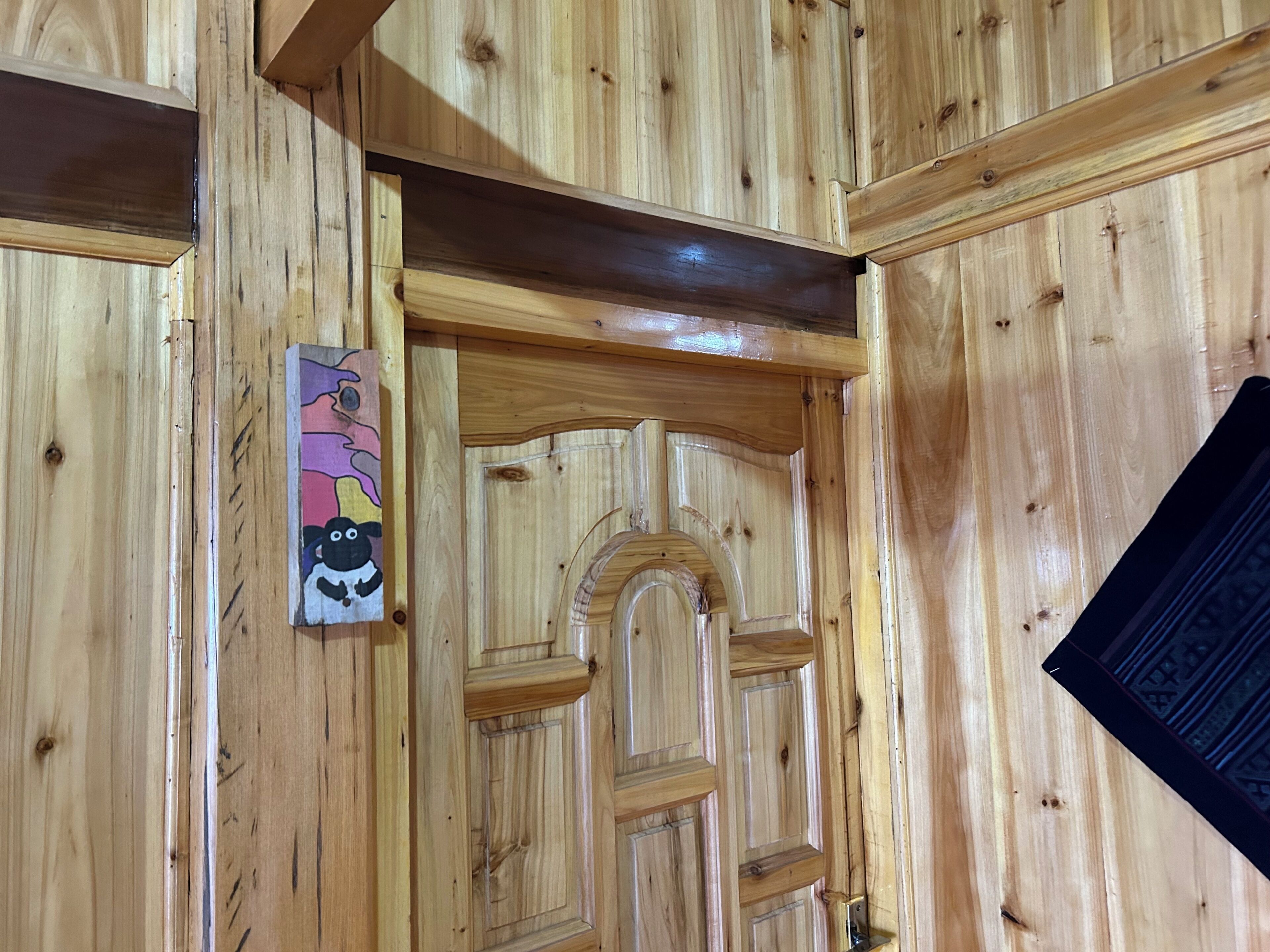 Une porte en bois ornée d’un arc décoratif, une petite œuvre d’art accrochée au mur et un objet noir sur la droite.