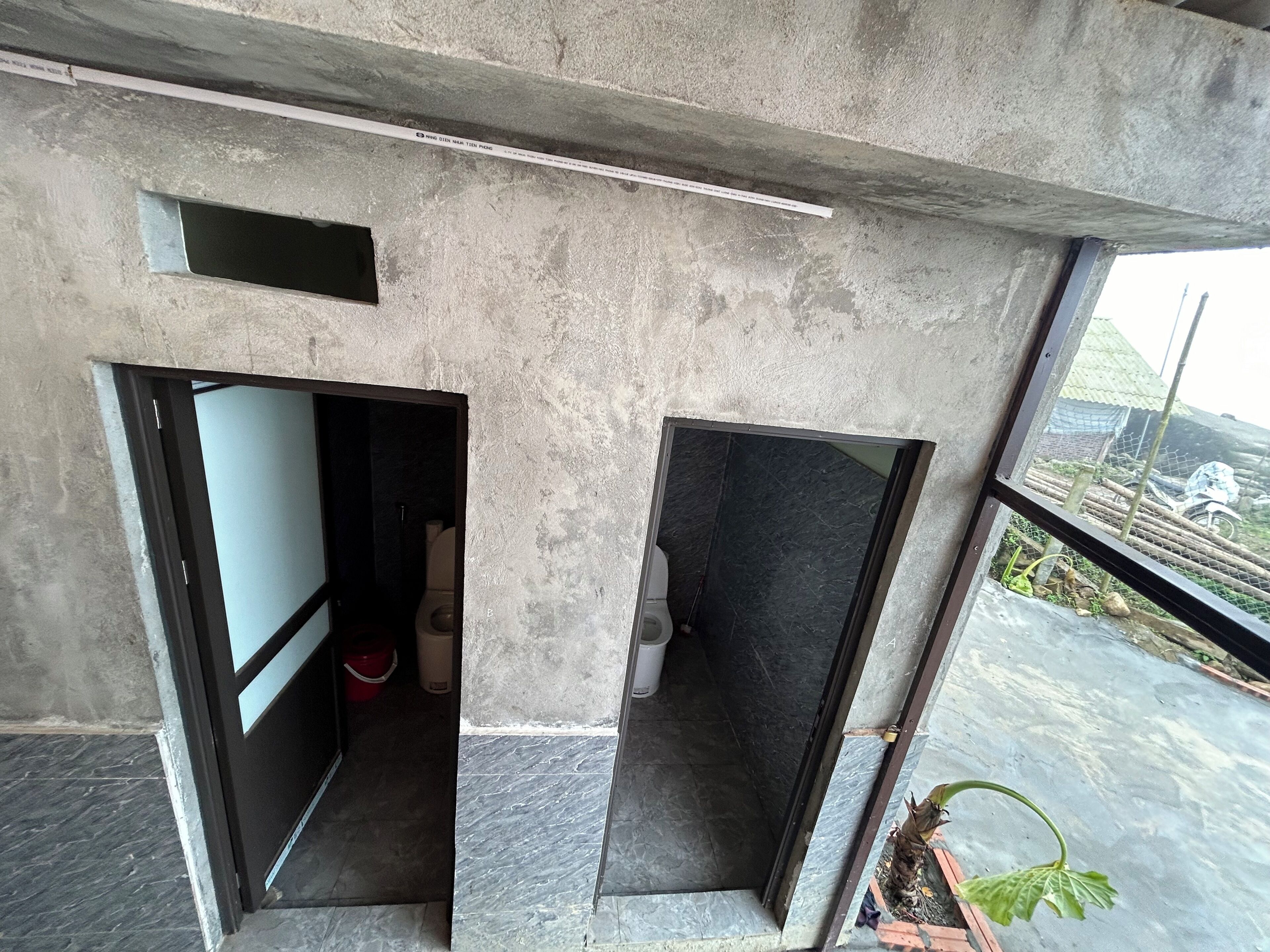 A room with a concrete ceiling, a window with a view of the outside, and a door leading to another room.