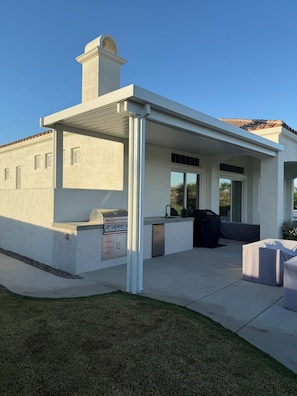 A modern outdoor kitchen with a grill, built-in sink, and seating area. - 3-bedroom estate in beautiful La Quinta with AC (La Quinta)