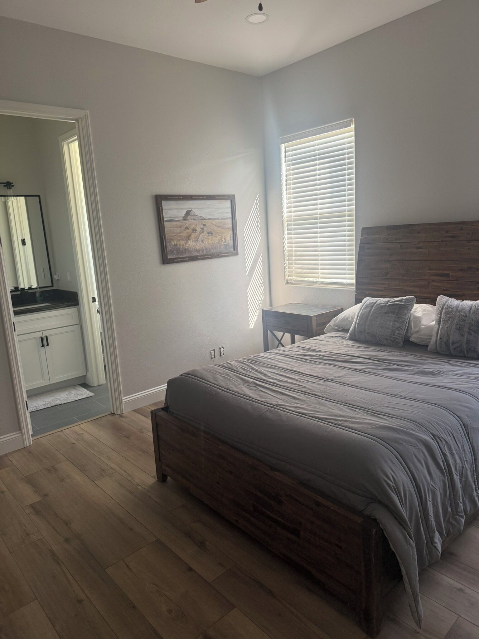 A bedroom with a bed, a nightstand, a window with blinds, a mirror, and a door leading to a bathroom.