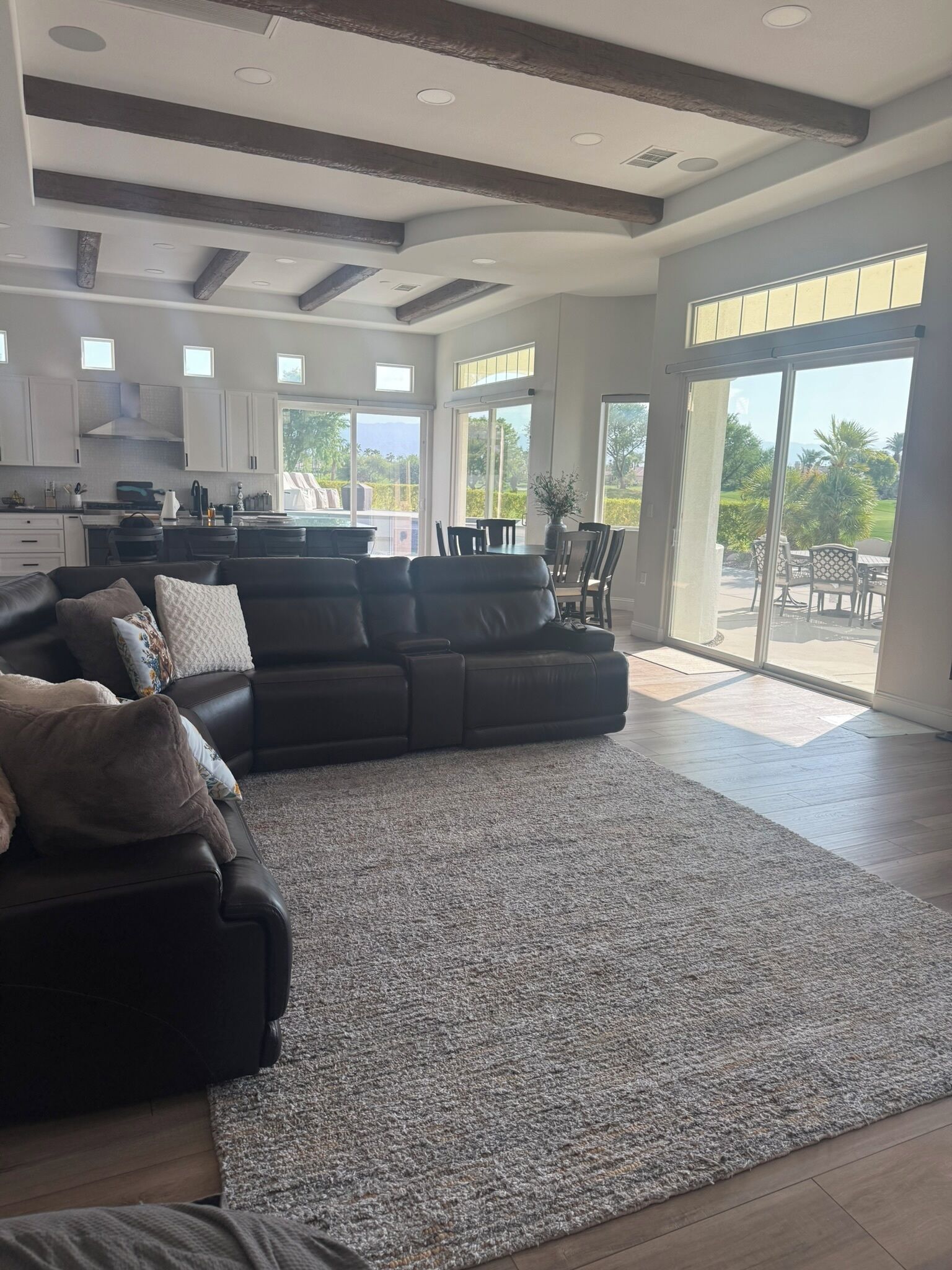 A spacious living room with a sectional sofa, a kitchen in the background, and a large sliding glass door leading to an outdoor patio.
