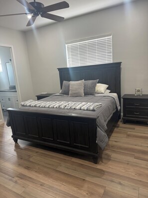 A bedroom with a dark wood bed, a ceiling fan, a window with blinds, a nightstand, and a dresser. - 3-bedroom estate in beautiful La Quinta with AC (La Quinta)