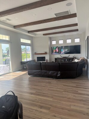A modern living room with a large sectional sofa, a flat-screen TV mounted on the wall, and a wooden ceiling with exposed beams. - 3-bedroom estate in beautiful La Quinta with AC (La Quinta)