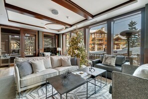A modern living room with a sofa, armchairs, and a coffee table. There is a large window with a view of a building and a Christmas tree. - Flagstaff Lodge Condo by InvitedHome | Ski-In/Out, Shuttle, Deer Valley, Apres (Park City)