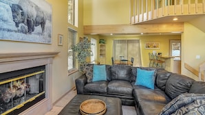 Een woonkamer met een open haard, een zwarte leren bank en een eethoek op de achtergrond.